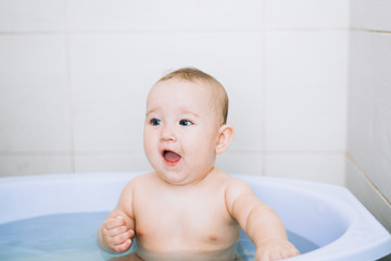 little girl baby is bathed in the blue basin in the bathroom is very fun