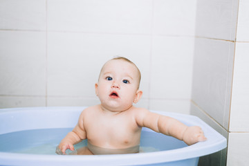 little girl baby is bathed in the blue basin in the bathroom is very fun