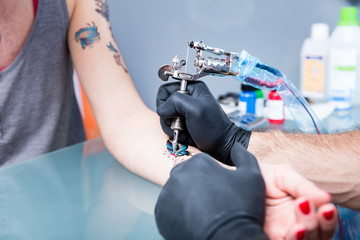 Close-up of the hands of a skilled tattoo artist wearing black gloves while setting a sterile...