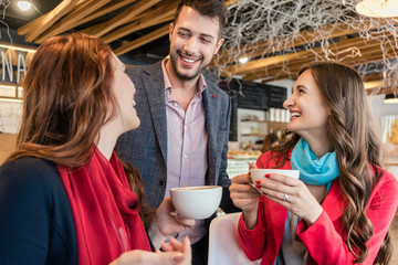 Attractive young woman meeting an old friend while sitting and enjoying a hot drink together with her best friend in a trendy coffee shop