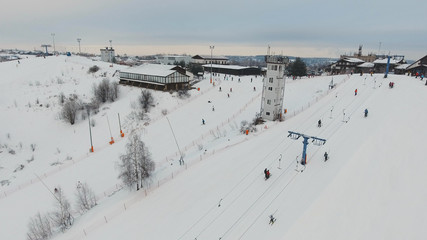 Aerial view: Skiers and snowboarders going down the slope in winter day. Skiers and snowboarders enjoying on slopes of ski resort in winter season.