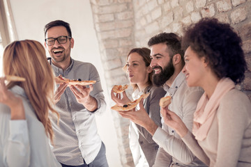 Happy young business team eating pizza in office
