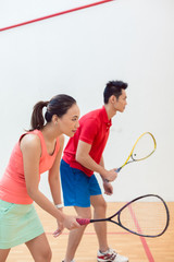 Side view of a beautiful and competitive Chinese woman holding the racquet while looking forward with concentration during a squash game with her partner
