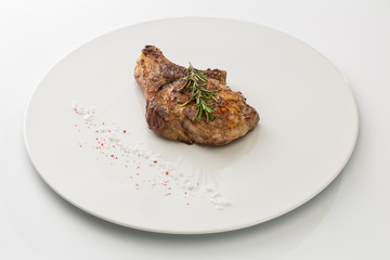 steak with salt and rosemary on a plate isolated on white background