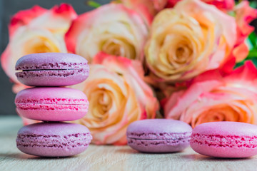 tender french macarons shades of pink on wooden table and rose background.