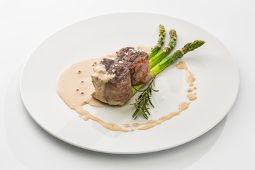 two pieces of shish kebab with sauce and asparagus on a plate isolated on white background