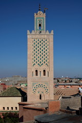 Minaret meczetu w Marrakeszu, Maroko, wysoko ponad dachami domów, misternie ozdobiony, niebieskie niebo