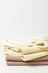 Multicolored clean towels on a light wooden background with copy space. Texture of cotton, waffle towel, textiles. Towels for kitchen or Spa concept.