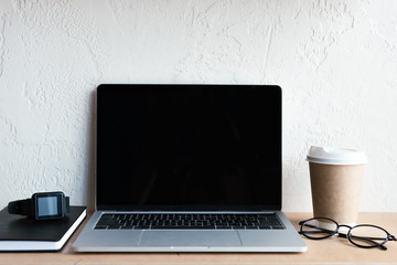 Fototapeta premium laptop with blank screen, smartwatch, notebook, eyeglasses and coffee to go on table