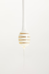 close up view of wooden honey deeper with organic honey on white background