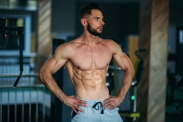 Fototapeta premium Young athlete posing with a torso for photography on a gym background. Bodybuilder, athlete with pumped muscles