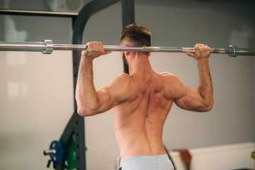 Fototapeta na wymiar A young athlete trains in the gym. Shows the muscles of the back and chest