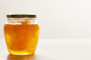 close up view of honey and beeswax in glass jar on white background
