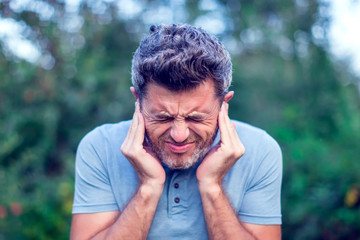 Male having ear pain touching his painful head outdoor