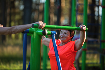 Mature woman on sport playground doing exercises on simulator.