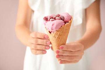 Woman holding waffle cone with delicious raspberry ice cream on color background, closeup