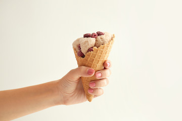 Woman holding waffle cone with delicious ice cream and raspberries on white background