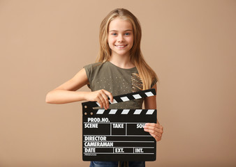 Cute little girl with clapper board on color background