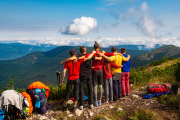 Hikers, friends stand, embracing on a mountain top