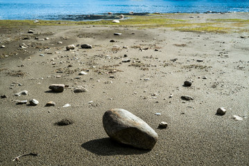 Many stones with different sizes on the beach in sunshine with seagrass and blue sea in the background in summer season