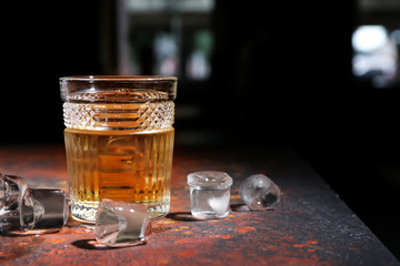 Glass of icy whiskey on color table