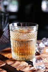 Glass of icy whiskey on wooden board
