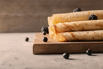 Delicious thin pancakes with berries on wooden board