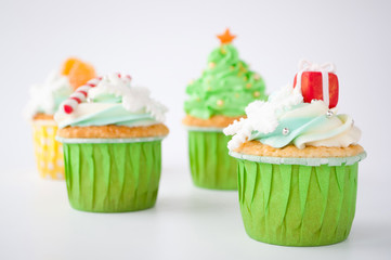 New year or christmas green cupcakes with whipped cream, decorated with a christmas tree, candy cane, a snowflake, a red box, tangerines, silver and gold confectionery balls on white background.