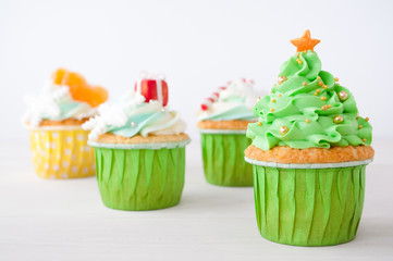 New year or christmas green cupcakes with whipped cream, decorated with a christmas tree, candy cane, a snowflake, a red box, tangerines, silver and gold confectionery balls on white background.