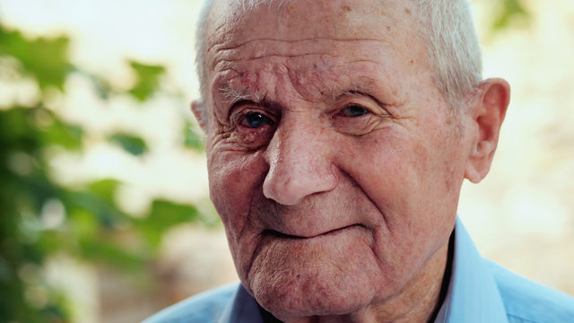 Very Old Man Portrait With Emotions. Grandfather Is Smiling And Looking To Camera. Portrait: Aged, Elderly, Senior. Close-up Of Old Man Sitting Alone Outdoors.