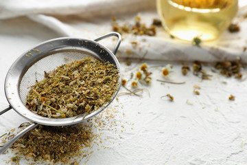 Sieve with dried chamomile flowers on white table, closeup