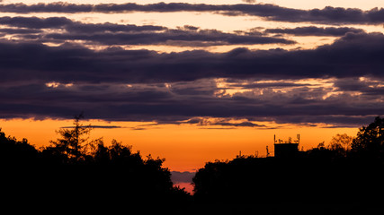 Sunset with silhouettes of trees and a building with many antennas with colorful clouds in the background