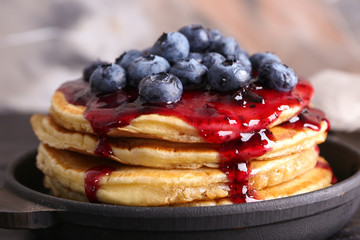 Frying pan with tasty pancakes, jam and blueberries on table, closeup