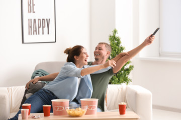 Couple fighting for remote control while watching TV at home