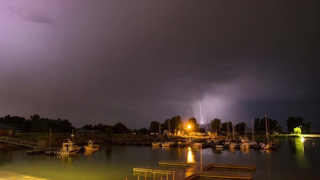 Time lapse of lightning flashing over boat harbor at night as clouds roll through the sky.