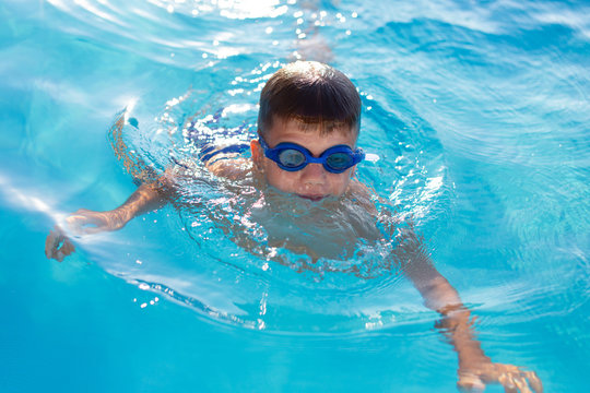 Young boy in goggles swim in swimming pool