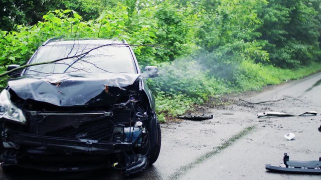 A broken car after an accident, smoke coming out from under the hood.