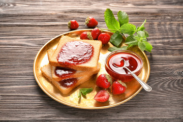 Plate with slices of bread and delicious strawberry jam on wooden table