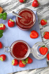 Glass jars with delicious strawberry jam on wooden table