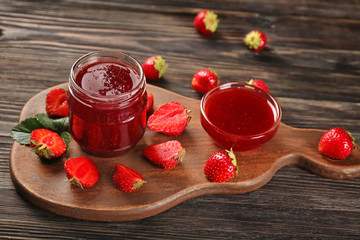 Glass jar and bowl with delicious strawberry jam on wooden table