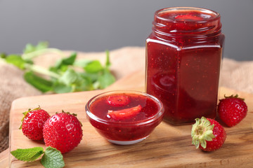 Glass jar with delicious strawberry jam on board
