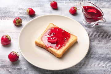 Plate with slice of bread and delicious strawberry jam on wooden table
