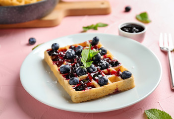Plate with delicious waffle and blueberry jam on color table