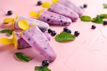 Tasty blueberry popsicles on color background