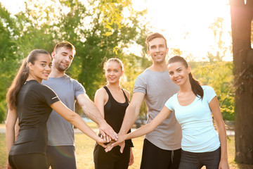 Group of sporty people putting hands together outdoors