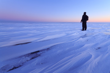 ice desert sunrise on a lake / man looking into the distance shortly before the dawn