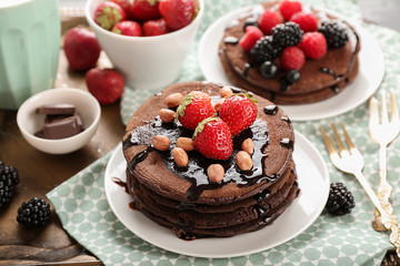Tasty chocolate pancakes with peanuts and strawberries on plate