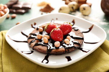 Tasty chocolate pancake with peanuts and strawberries on plate