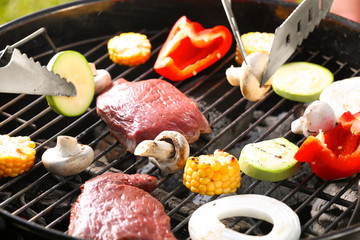Tasty steaks and vegetables cooking on barbecue grill, closeup