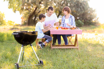 Barbecue grill with tasty food near family having picnic in park